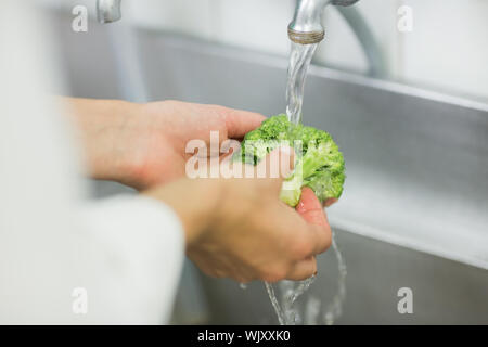 Chef broccoli di lavaggio sotto il rubinetto in una cucina commerciale Foto Stock