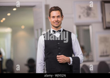 Bello il cameriere sorridente in telecamera in un lussuoso ristorante Foto Stock