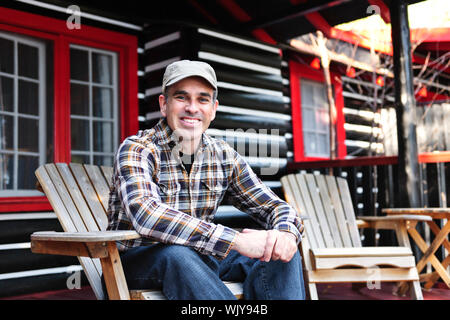 Uomo sorridente seduto sul ponte cottage in legno sedia adirondack Foto Stock