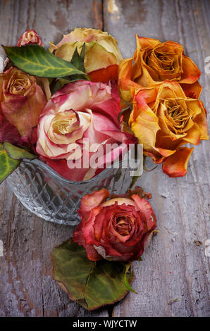 Mazzetto di colorati rose appassite in vaso di vetro isolato sul rustico sfondo di legno Foto Stock