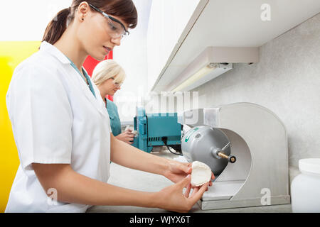 Vista laterale dei tecnici di sesso femminile utilizzando la levigatura impronte dentali Foto Stock