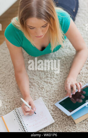 Donna sdraiata sul pavimento facendo il suo dovere utilizzando tablet Foto Stock