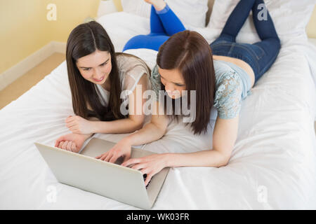 Happy amici usando un computer portatile giacente sul letto Foto Stock