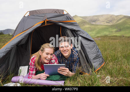 Sorridente giovane giacente nella loro tenda e con tavoletta digitale Foto Stock