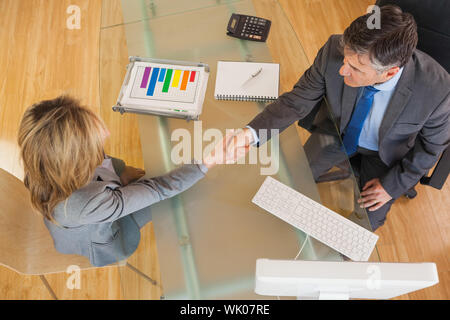 Due persone di affari avente una stretta di mano sopra una scrivania Foto Stock