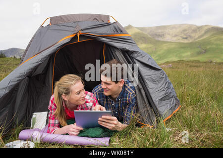 Coppia felice giacente nella loro tenda e con tavoletta digitale Foto Stock