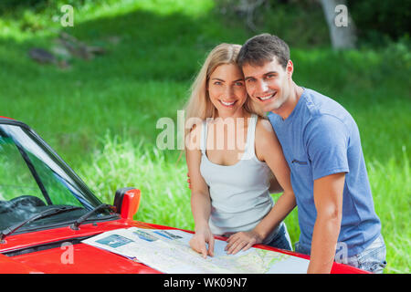 Felice coppia giovane lettura mappa sulla loro cabriolet cofano Foto Stock