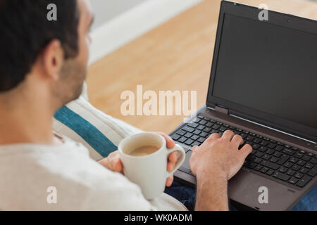Marrone uomo dai capelli tenendo il caffè usando il suo computer portatile Foto Stock