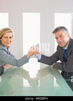 Due imprenditori sorridente avente un showdown seduti attorno a un tavolo Foto Stock