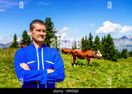 Pastore in piedi di fronte di vacche in montagne alpine Foto Stock