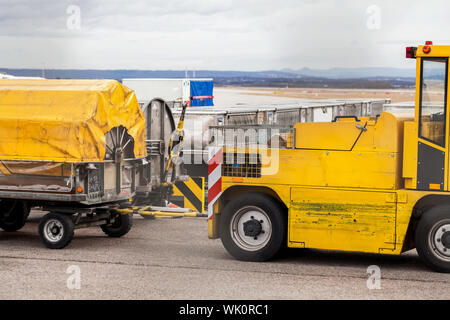 Carrelli caricati con i bagagli in un aeroporto in piedi su asfalto sotto giallo teloni in attesa di essere caricato su un aereo Foto Stock