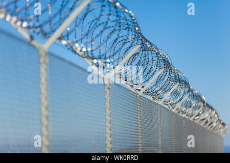 Avvolto il filo di rasoio sulla parte superiore di una recinzione Foto Stock