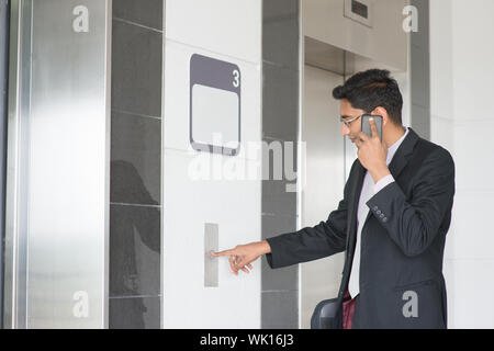 Asian commerciante indiano premendo sul pulsante di ascensore, in attesa porta aperta per accedere all'interno dell'ascensore. Foto Stock