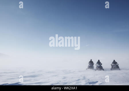 Tre motoslitte su un soffiaggio brullo paesaggio invernale Foto Stock