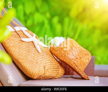 Estate accessori, cappello di paglia e la borsa decorata con starfish sdraiato sul lettino nel giardino sul beach resort, viaggi e turismo concept Foto Stock