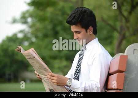 Commerciante indiano la lettura di un quotidiano in un prato Foto Stock