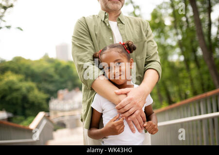 Bella dark-eyed figlia con capelli panini in piedi con padre Foto Stock