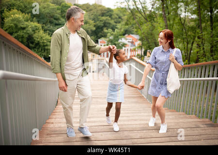 Allegro con la pelle scura la figlia a parlare e a piedi con i genitori Foto Stock