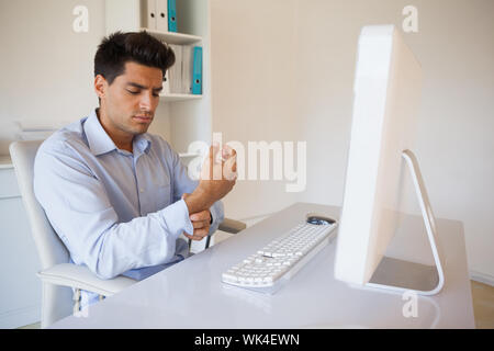 Imprenditore Casual toccando il suo polso dolente nel suo ufficio Foto Stock