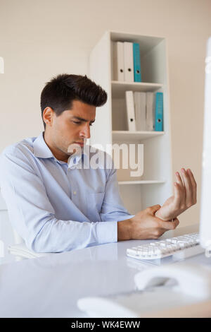 Imprenditore Casual toccando il suo polso dolente nel suo ufficio Foto Stock