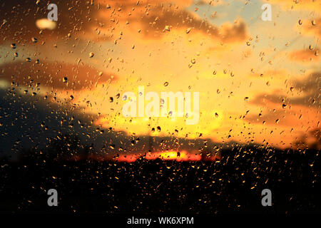 La pioggia al di fuori della finestra sul background del tramonto. Gocce di pioggia sul vetro durante la pioggia. Tramonto al di fuori finestra durante la pioggia. Texture brillanti di gocce di acqua Foto Stock