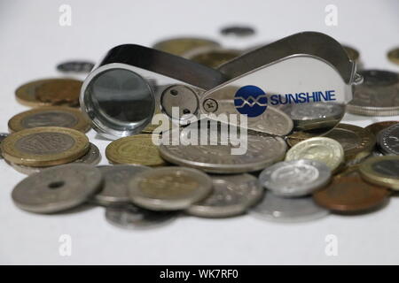 Monete internazionali assortite con lente d'ingrandimento di un gioielliere per l'ispezione e la raccolta delle valute Foto Stock