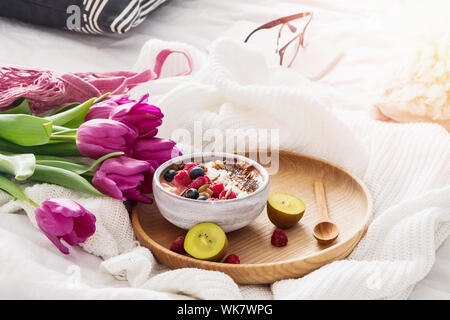 Ciotola Smoothie e tulipani viola sullo sfondo sul letto bianco Foto Stock