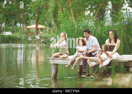 Giovane famiglia felice con i ragazzi con attività di pesca in stagno in estate Foto Stock