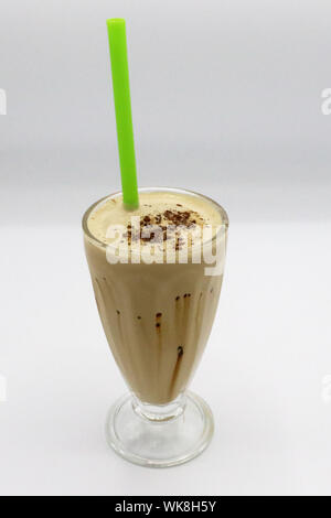 Frullato di caffè freddo servito in un bicchiere alto con paglia verde, ricoperto di cacao in polvere e gocciolatoio di cioccolato. Foto Stock