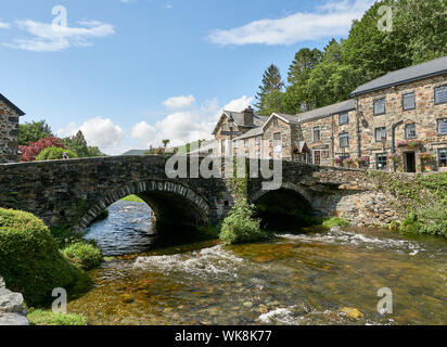 Vista di un ponte di pietra sul fiume Glaslyn che scorre attraverso la città di Beddgelert su una giornata d'estate, Snowdonia, Gwynedd, Wales, Regno Unito Foto Stock