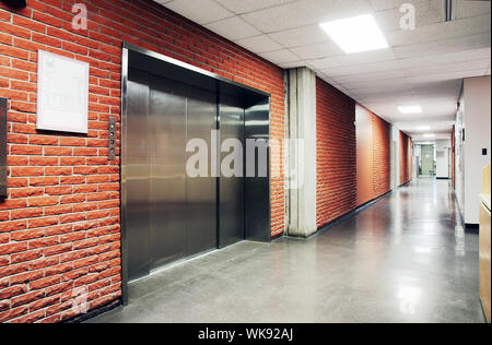 Un nolo lo sportello in acciaio inox ascensore circondato da brcik parete di un corridoio deserta. Potrebbe essere ufficio, scuola, casa di riposo e ospedale. Foto Stock