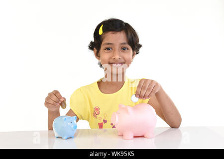 Ragazza mettendo moneta in piggy banche Foto Stock