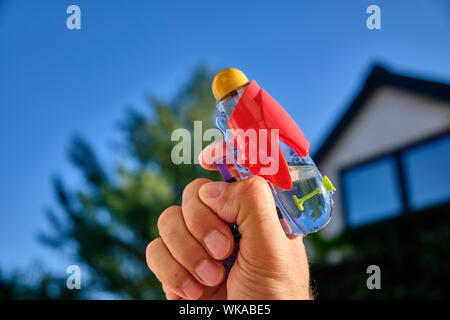 Un colorato acqua pistola in un maschio caucasico mano nella parte anteriore di una casa e il cielo blu di una soleggiata giornata estiva Foto Stock