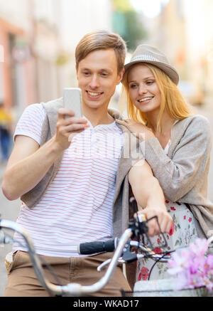 Vacanze estive, biciclette, amore, relazione, navigazione gps e concetto di dating - giovane con le biciclette e lo smartphone nella città Foto Stock