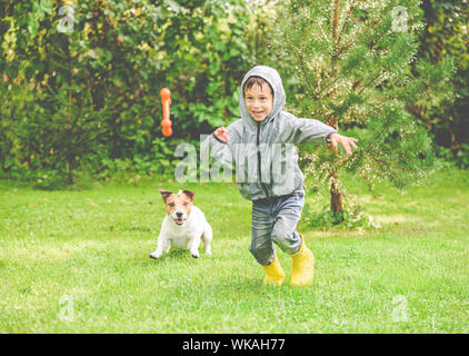 Cane giocando con il ragazzo sotto la pioggia a backyard prato Foto Stock