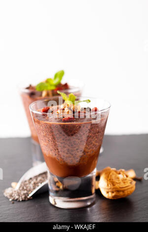 Cibo sano concetto Chia semi, cioccolato budino di latte con goji secche e le noci a piccoli vetro su ardesia nera sullo sfondo della scheda Foto Stock