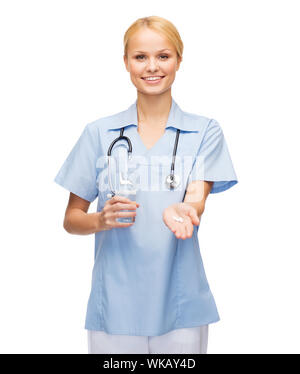 Salute, medicina e farmacia concetto - sorridente medico o infermiere con uno stetoscopio offrendo pillole e bicchiere di acqua Foto Stock