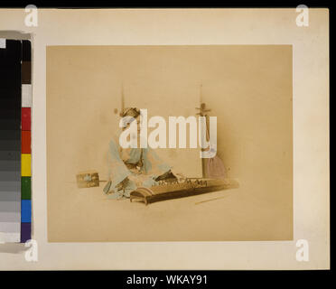 Donna Giapponese a piena lunghezza, seduto, rivolto verso destra, la riproduzione di un koto; un shamisen appoggia contro una parete in background Foto Stock