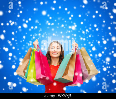 Shopping, vendita, regali di Natale, X-mas concetto - Donna sorridente in abito rosso con colorati borse per lo shopping Foto Stock