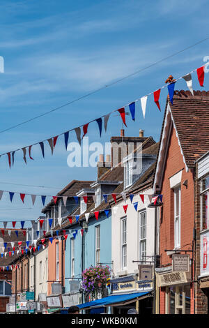 Classic estate English street con vivacemente colorati negozi e case con bunting infilate al di là della strada. Foto Stock