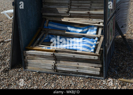 Brighton, Regno Unito, 2019-08-29. Close up della striscia blu lettini per prendere il sole sulla spiaggia di pietra essendo memorizzato tra usi Foto Stock