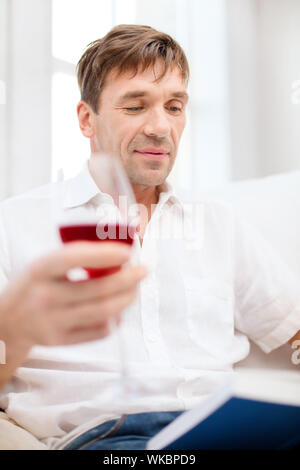 Tempo libero, bevande, pensionamento, istruzione e concetto di stile di vita - uomo felice con libro e un bicchiere di vino rosso a casa Foto Stock