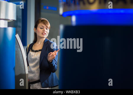 Piuttosto, giovane donna il ritiro di denaro dalla sua carta di credito presso uno sportello ATM (SHALLOW DOF; dai toni di colore immagine) Foto Stock