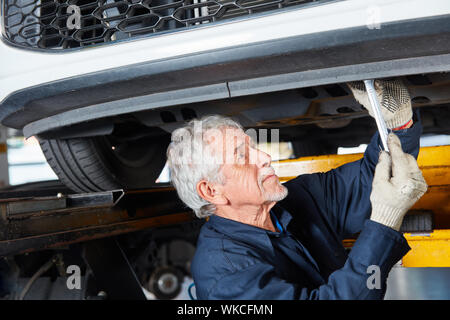 Meccanico esperto ispeziona o riparazioni auto su sollevamento in officina Foto Stock