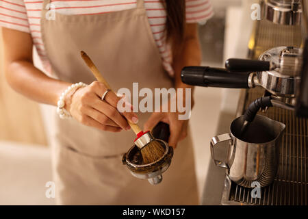 Utilizzando una speciale spazzola. Duro lavoro barista utilizzando pennello speciale durante la pulizia di parti di macchina per il caffè Foto Stock