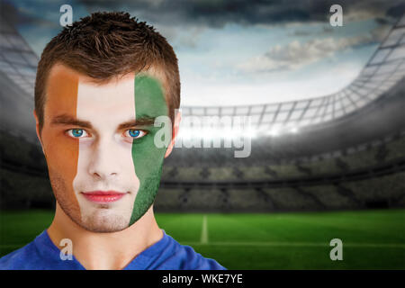 Immagine composita della Costa d'Avorio appassionato di calcio in faccia vernice contro grande stadio di calcio con luci Foto Stock