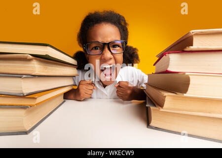 Scuola elementare ragazza seduta che urlavano tra pile di libri in Studio Foto Stock