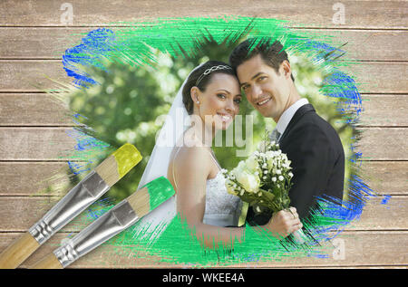 Immagine composita di sposi sorridente in telecamera con pennello immerso nel verde su una superficie di legno con tavole Foto Stock