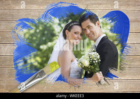 Immagine composita di sposi sorridente in telecamera con pennello immerso in giallo contro la superficie di legno con tavole Foto Stock