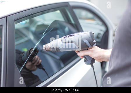 Lavoratore rimozione auto finestra foglio di pellicola utilizzando la pistola ad aria calda. Foto Stock